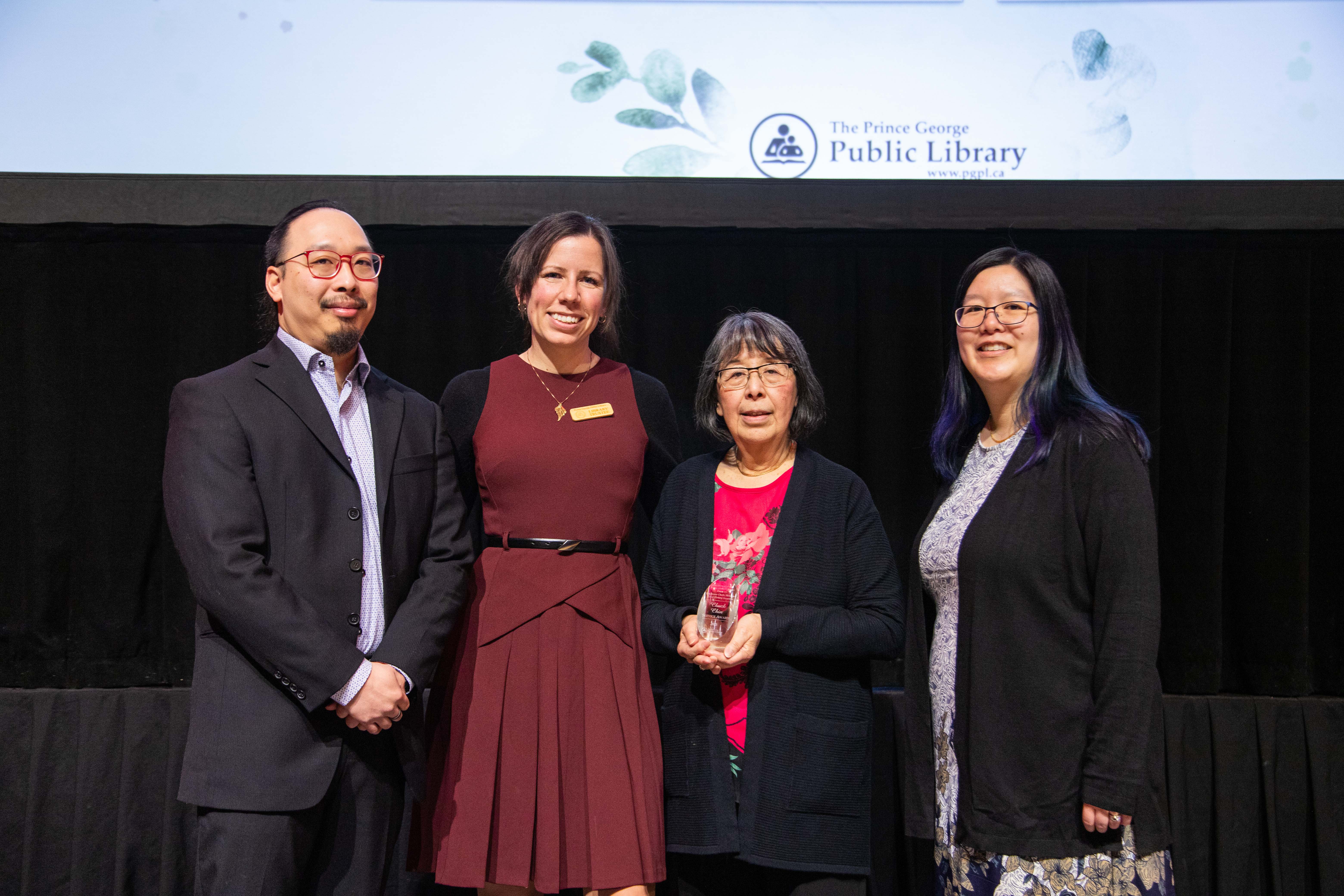 Four people standing on a stage and smiling at the camera.