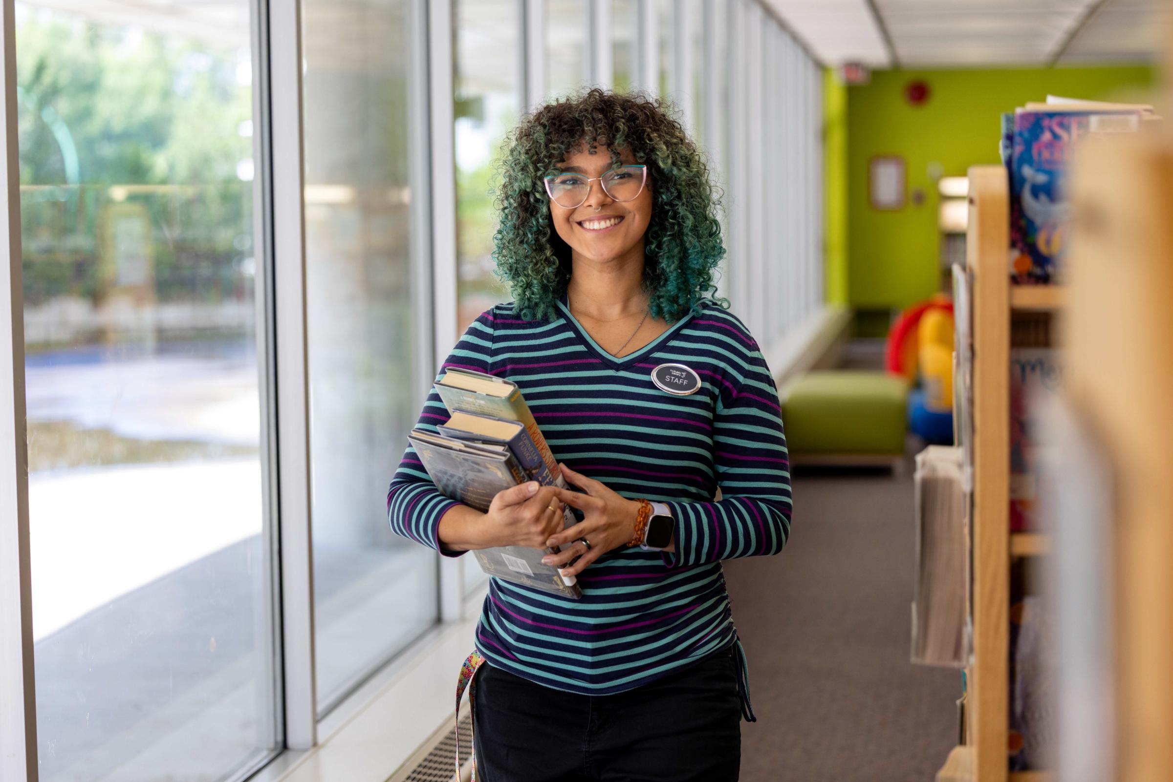 A smiling person holding a stack of books in their hands.