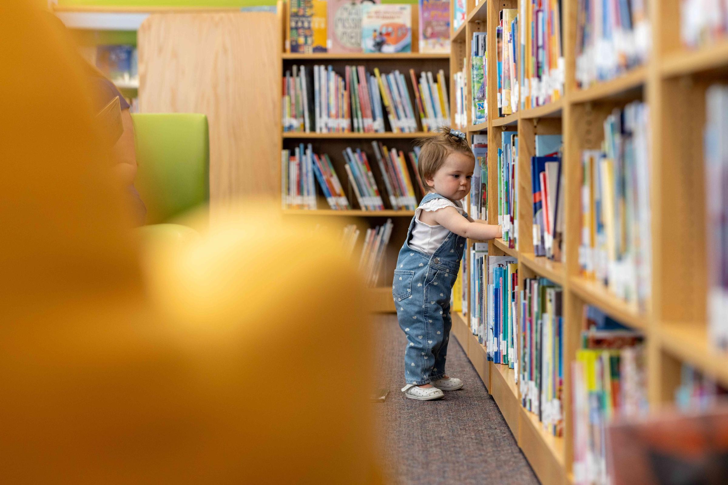 Small child reaching for books on a book shelf.