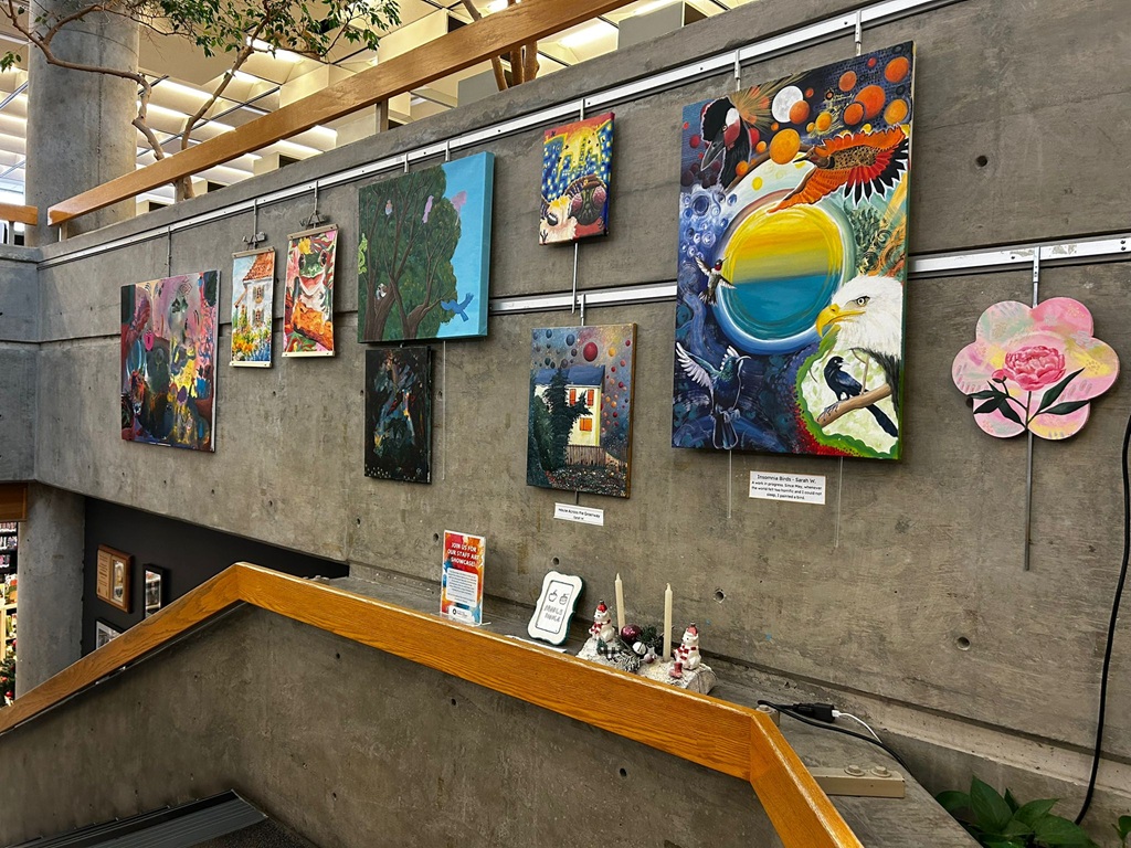 Canvas paintings and sketches on a wall adjacent to a stairwell.